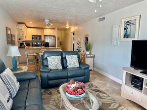 A living room with a sofa, a coffee table with decorative items, a television, and a kitchen in the background. - Island Beach Club 21 - Anna Maria Island - Condo 2 Bedroom / 2 Bath gulf front , maximum occupancy of 4 people. (Holmes Beach)