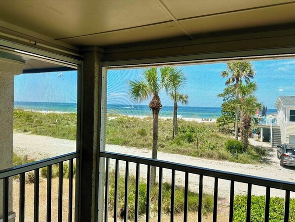 A balcony with a view of the beach, palm trees, and a house.