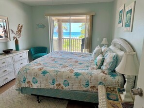A bedroom with a bed, a chair, a dresser, and a view of the ocean through a large window.