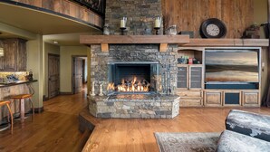 Une cheminée en pierre avec un feu de bois, un plancher en bois, un coin bar et un grand écran de télévision.