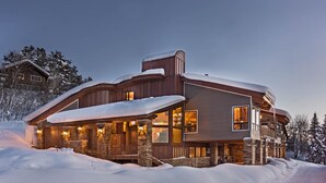 Un grand chalet à plusieurs étages, doté d’une façade en pierre et de détails en bois, entouré de neige.