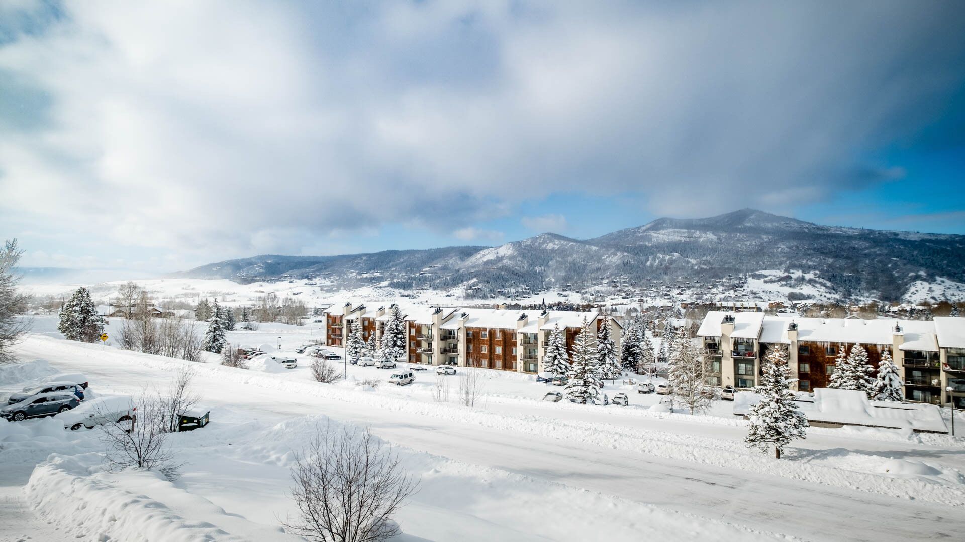 Un pueblo cubierto de nieve con edificios modernos, cielo despejado y vistas a montañas distantes.