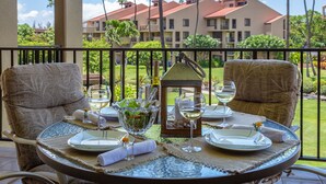 Un tavolo da pranzo apparecchiato con piatti, bicchieri e un centrotavola a candela su un balcone con vista su un resort con palme e edifici.