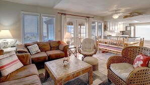 Ein Wohnzimmer mit braunem Ledersofa, einem Korbstuhl, einem Holztisch und einem Essbereich mit Holztable und Stühlen.