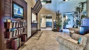 Eine großzügige Lobby mit hoher Decke, einem an einer Holzwand befestigten Fernseher, einem Empfangstresen und mehreren Zimmerpflanzen.
