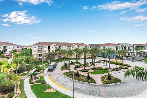 A residential complex with multiple apartment buildings, a central landscaped area with palm trees, and a curved road.