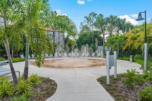 Une fontaine entourée de palmiers et un sentier menant à des espaces aménagés pour s’asseoir.