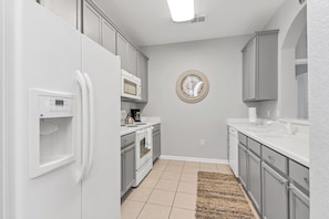 A kitchen with white appliances, grey cabinets, a microwave, and a round mirror on the wall. - 3BR Condo w/ Views, Pool Access near Epic Universe (Orlando)