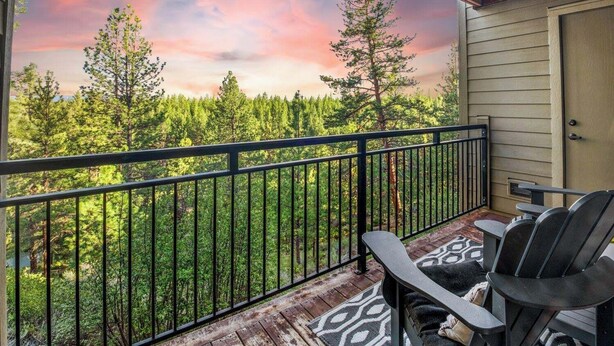 A balcony with a view of a forest, a wooden deck, and two Adirondack chairs. - Modern 3-bedroom Seventh Mountain Resort Condo (Bend)
