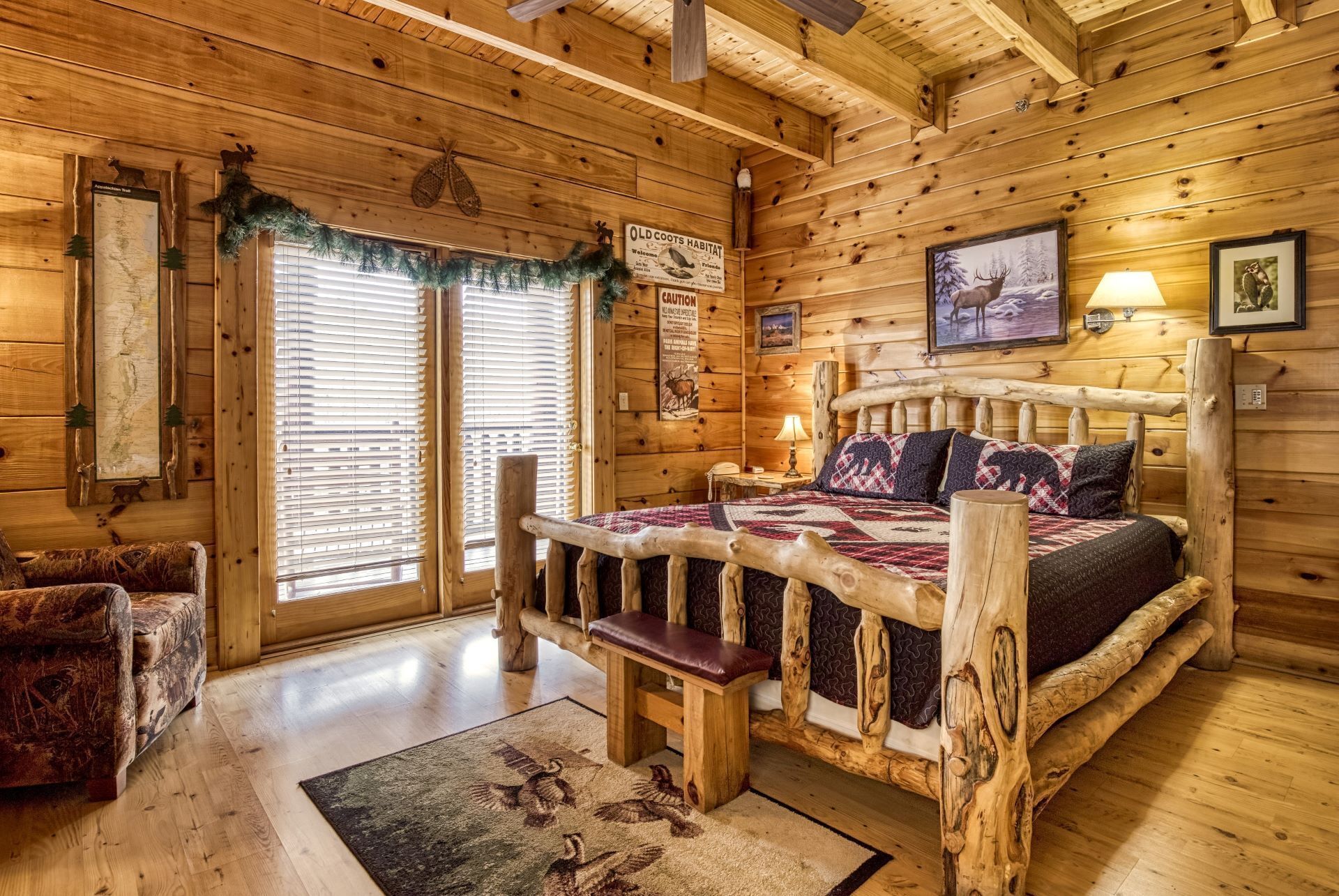 Une chambre dans un chalet en rondins, avec un lit en bois, un banc, une carte accrochée au mur et une fenêtre avec des stores.