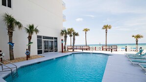 A swimming pool with a view of the beach, surrounded by palm trees and lounge chairs.