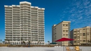 A high-rise hotel with multiple balconies, located near a beach with lounge chairs and umbrellas.