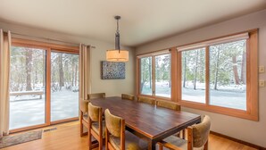 Un comedor con una gran mesa de madera, seis sillas y ventanas amplias que dan a una vista nevada.