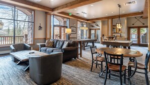A spacious living area with a large wooden table, comfortable seating, and large windows offering views of the outdoors.