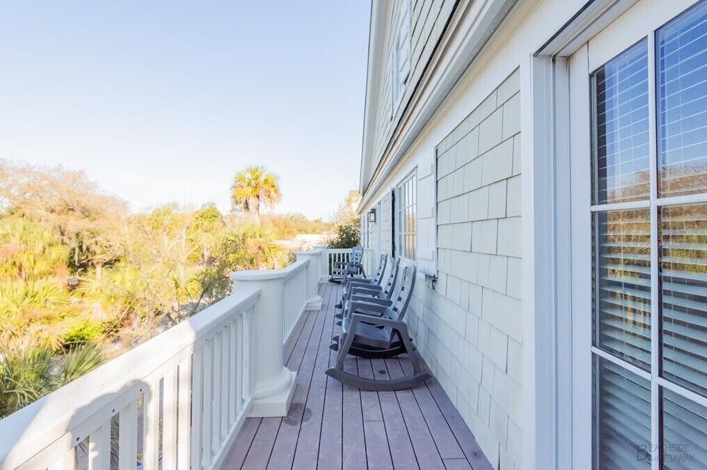 A wooden deck with rocking chairs, a white railing, and a view of the surrounding landscape.