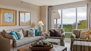 A living room with a sofa, armchairs, a coffee table, and a view of the sea.