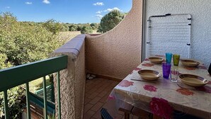 A balcony with a table set for dining, a whiteboard, and a view of greenery.