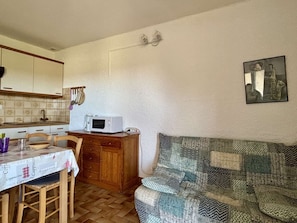 Uma cozinha compacta com micro-ondas, armários de madeira, uma mesa de jantar com cadeiras e um sofá estampado.