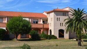 A two-story building with a red-tiled roof, a covered courtyard, and a palm tree.