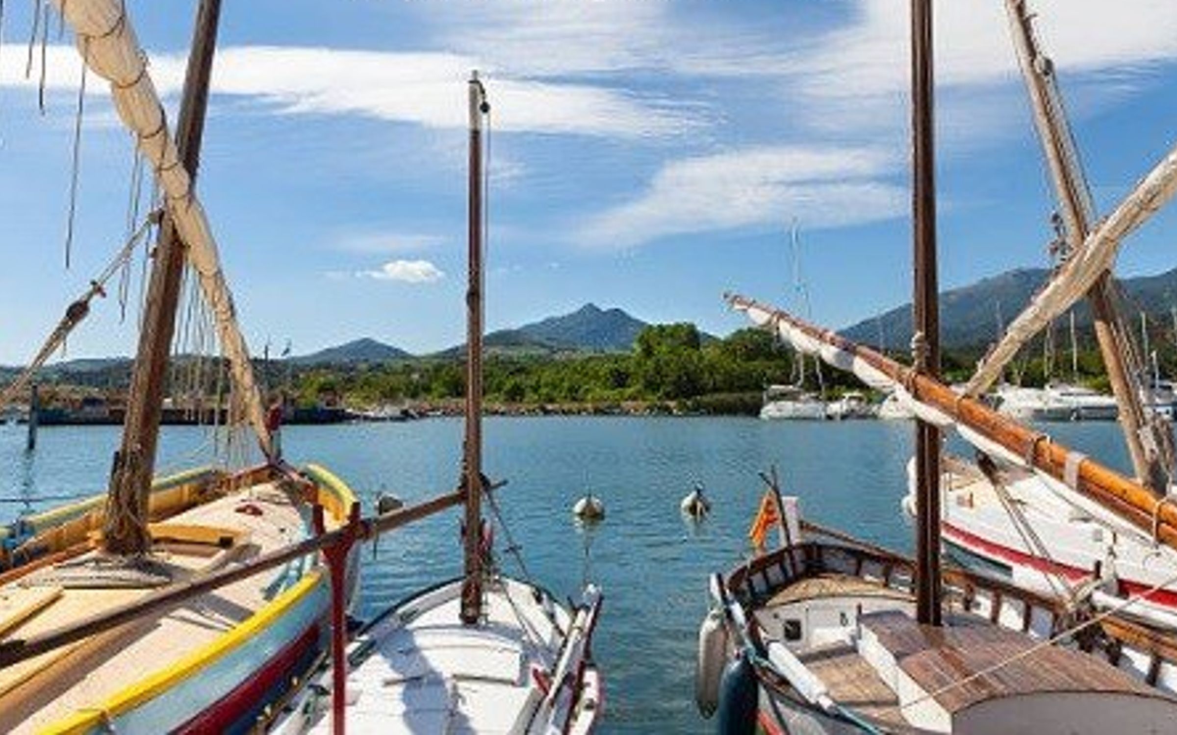 A harbor with several boats docked, a clear sky, and mountains in the background.