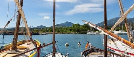 Un puerto con varias embarcaciones amarradas, cielo despejado y montañas al fondo.