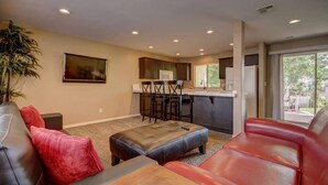 A living room with a sofa, ottoman, and a dining area with chairs and a kitchen in the background.