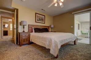 A bedroom with a large bed, two bedside tables, a ceiling fan, and a door leading to a balcony.