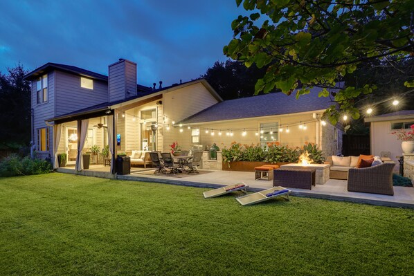 Een modern huis met een patio, voorzien van buitenmeubilair, een vuurkorf en lichtjes.
