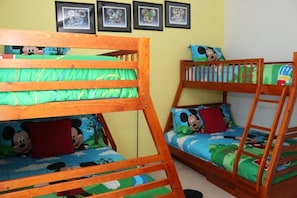 Une chambre avec des lits superposés, dotée de draps à l’effigie de Mickey Mouse, de tableaux encadrés accrochés au mur et d’une échelle fixée à l’un des lits.