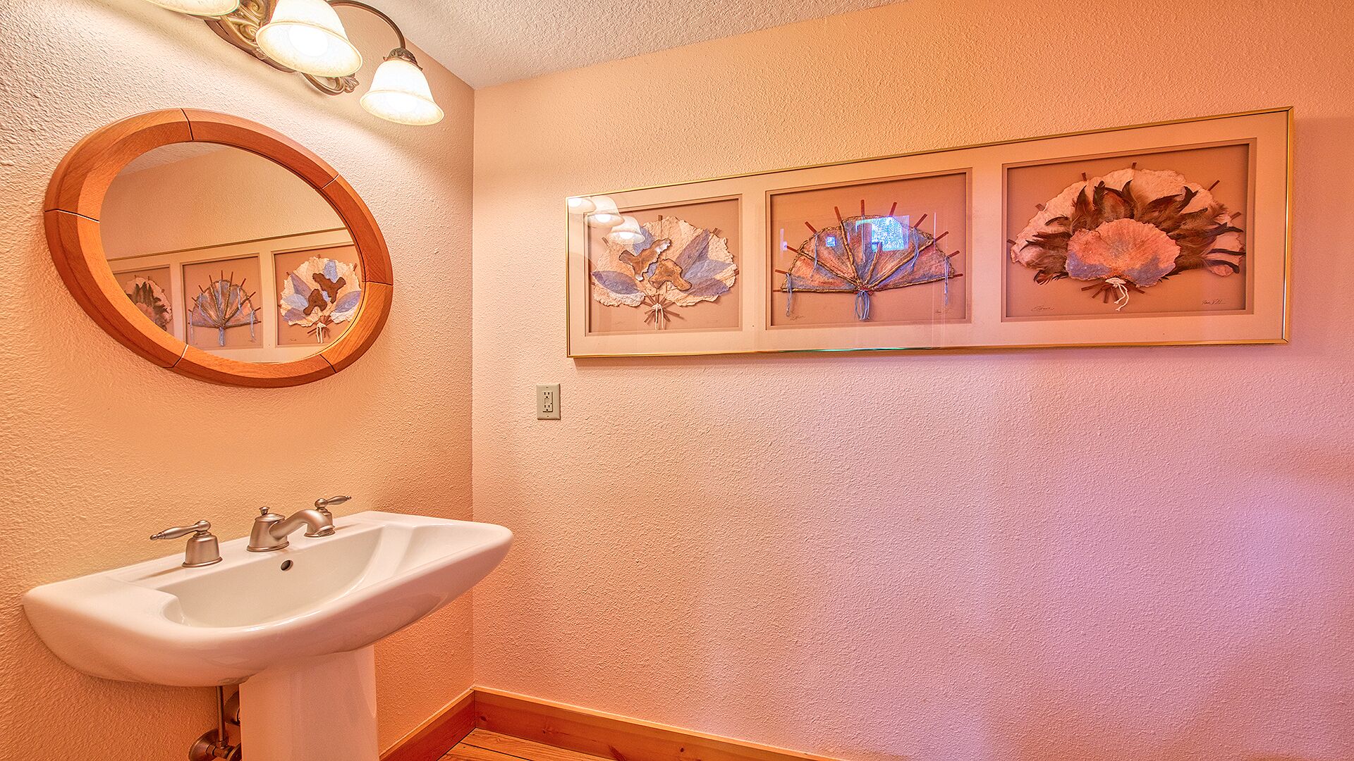 A bathroom with a white sink, a round mirror, and three framed wall art pieces.