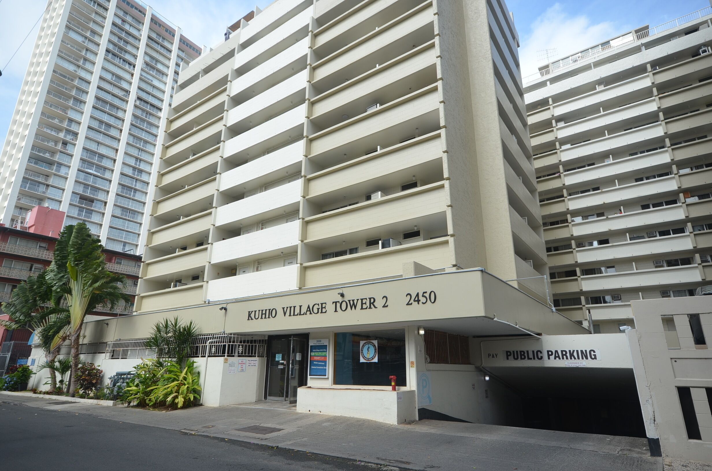 Un immeuble à plusieurs étages portant une enseigne indiquant « KUHIO VILLAGE TOWER 2 2450 » et « PARCING PUBLIC ».