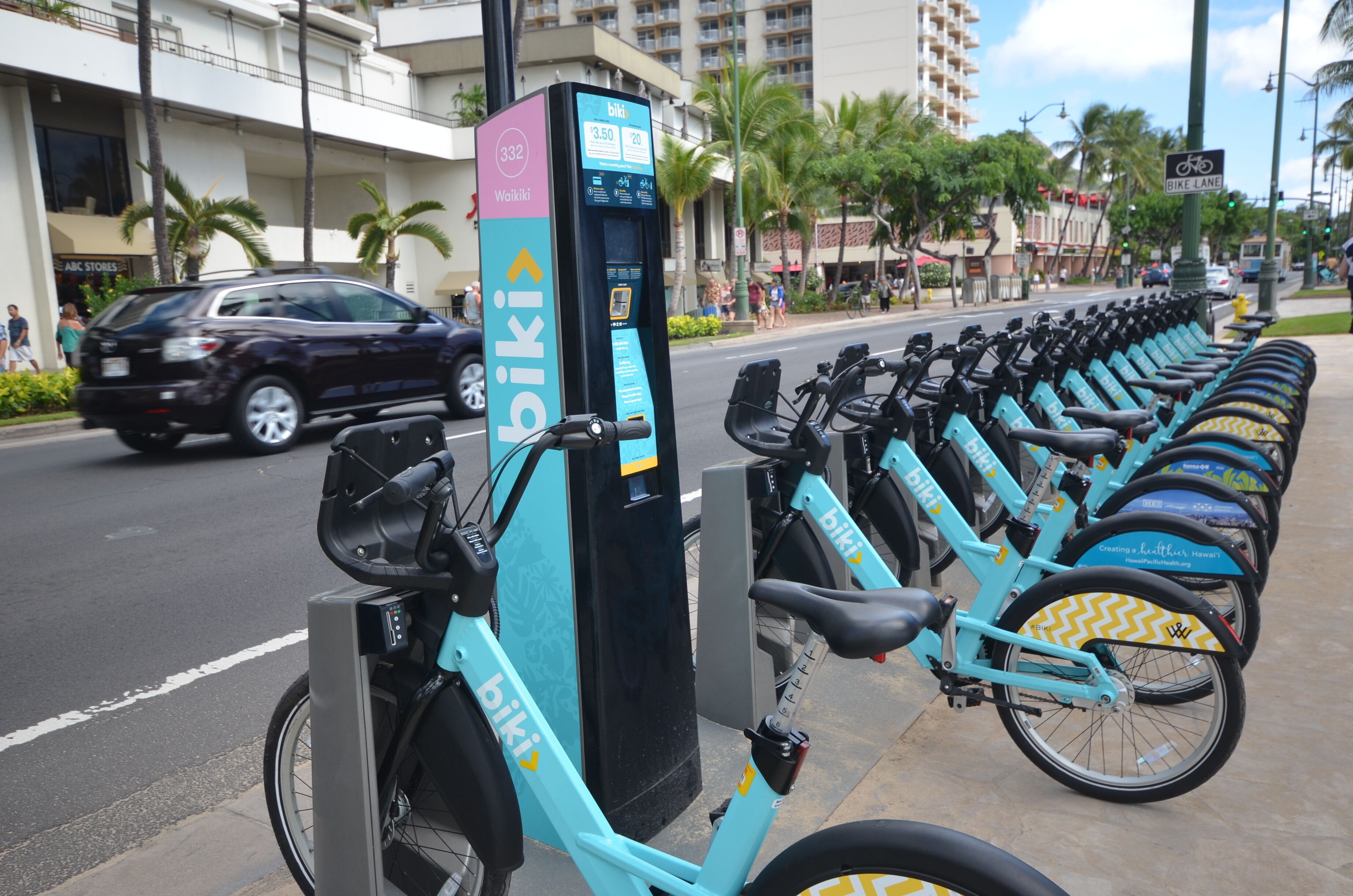 Une rangée de vélos est garée à côté d’une station de location de vélos, qui est équipée d’un écran numérique.