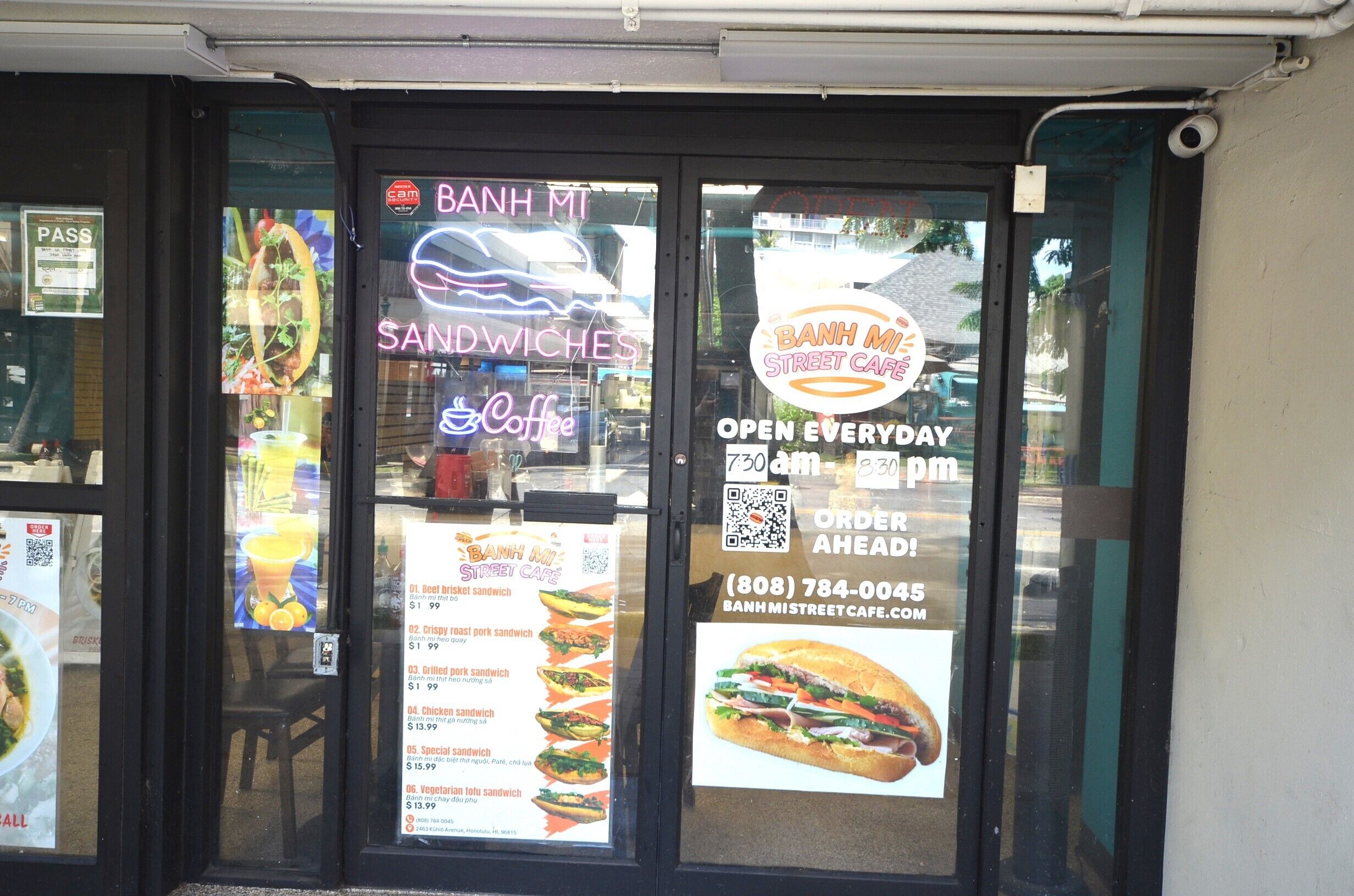 Un café en la calle con un cartel que muestra varios sándwiches y precios.