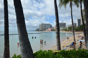A beach with palm trees, a sandy shore, and a view of high-rise buildings in the background. - Kuhio Village 803A - Waikiki Private Getaway - 2 mins to Waikiki Beach (Honolulu)