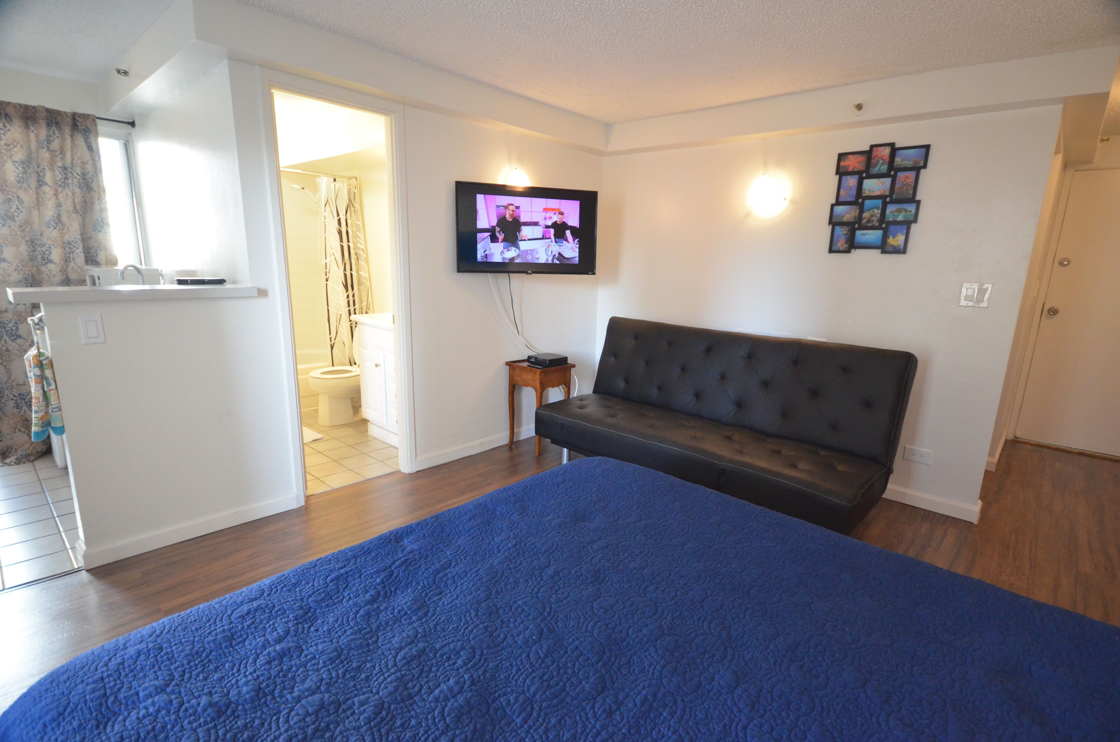 A bedroom with a bed, a television on the wall, a small table, and a door leading to the bathroom.