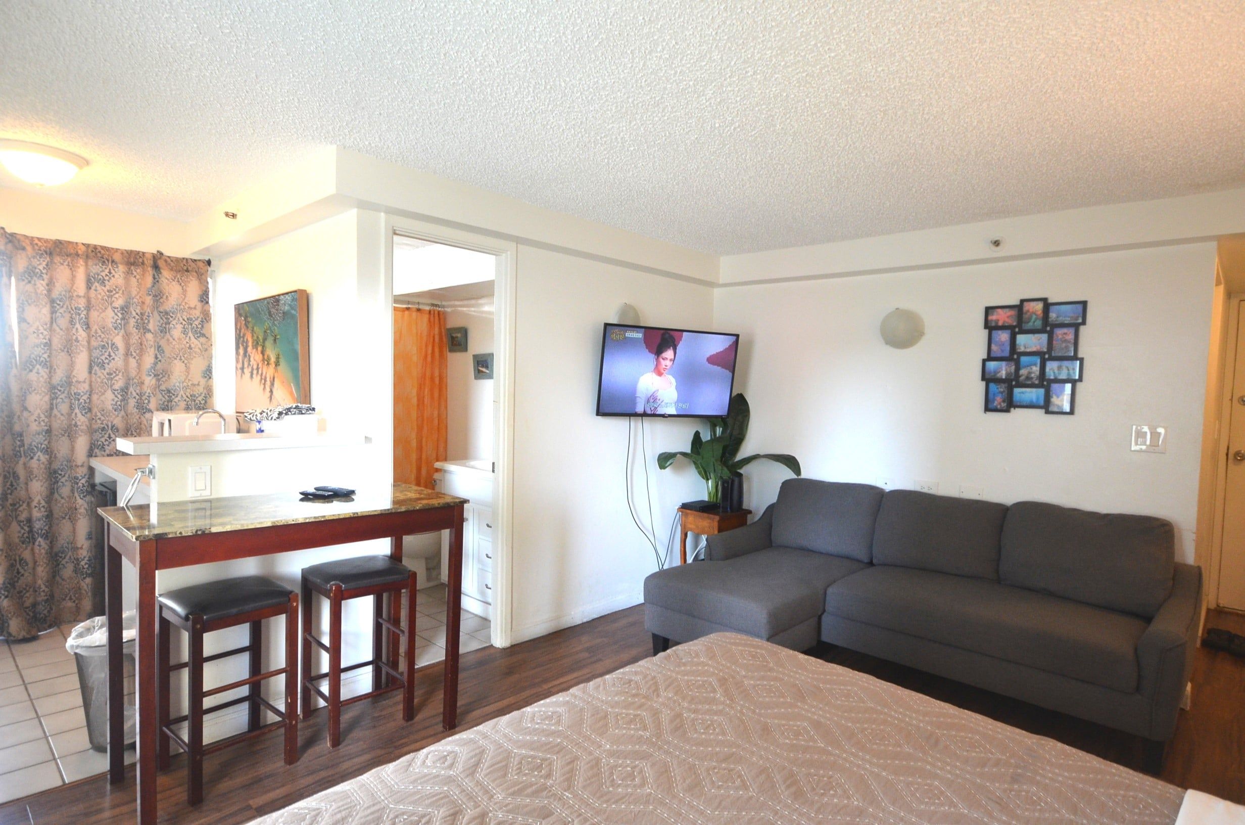 Una habitación de hotel con cama, sofá, televisor, mesa de comedor con sillas y un baño visible a través de una puerta abierta.