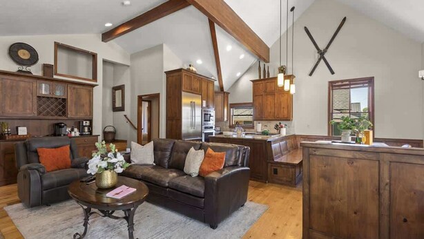 A spacious living area with a dark leather sofa, wooden cabinets, and a kitchen in the background.