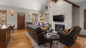 A spacious living room with a fireplace, leather sofas, a flat-screen TV, and a wooden ceiling.