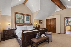Une chambre à coucher avec un grand lit, une tête de lit en bois, une table de chevet, un banc, une valise et une armoire.
