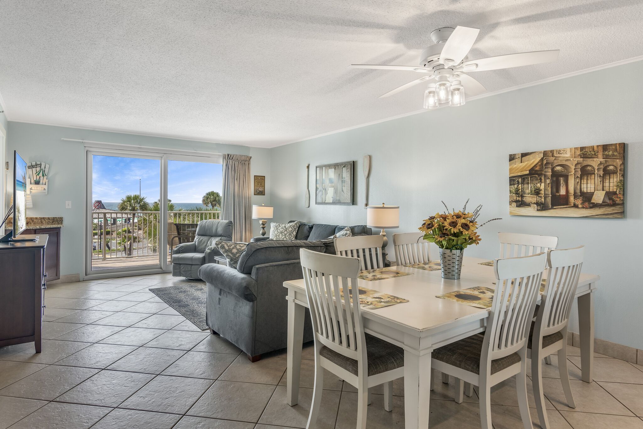 A spacious living area with a dining table, grey sofa, and a balcony with a view.