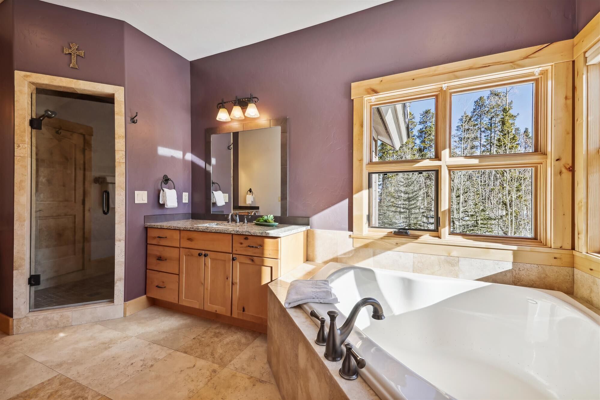 A modern bathroom with a large bathtub, wooden cabinets, a vanity, and a large window with a forest view.
