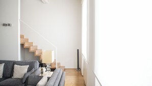 Een moderne woonkamer met een grijze bank, een houten trap en een vloerlamp.