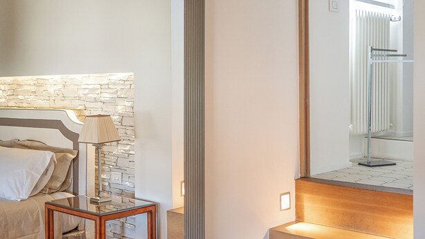 Een slaapkamer met een stenen hoofdbord, een nachtkastje, een lamp en een grote spiegel.