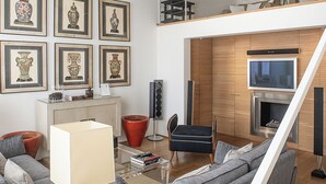 Een moderne woonkamer met een grijze bank, een salontafel, een televisie en kunstwerken in lijsten aan de muur.
