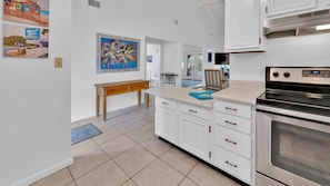 A kitchen with white cabinets, a wooden bench, a painting, and a Whirlpool stove. - Chateau La Mer 9D | Private Beach | FREE Seasonal Activities (Destin)