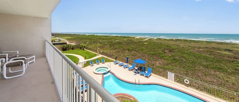 Un balcon avec vue sur la plage et une piscine dotée de chaises longues.