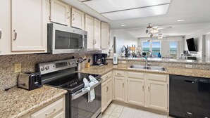 A modern kitchen with a built-in microwave, stove, and dishwasher, granite countertops, and a large window overlooking the ocean. - Edgewater 304 Sandy Beach and a heated swimming pool. (South Padre Island)