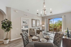 A modern living room with a dining area, a chandelier, a large window with a view, and a potted plant.