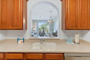 A kitchen with wooden cabinets, a double sink, and a view into the living area. - Chic 2BR Condo w Balcony Near Epic Universe (Orlando)