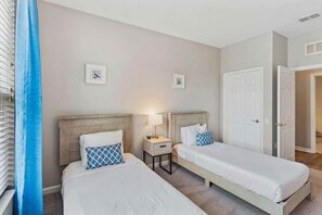 Et hotelværelse med to enkeltsenge, et natbord med lampe og en dør til et andet rum.